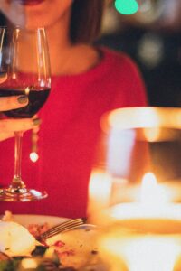 A woman enjoying red wine at a romantic candlelit dinner, perfect for celebrations.